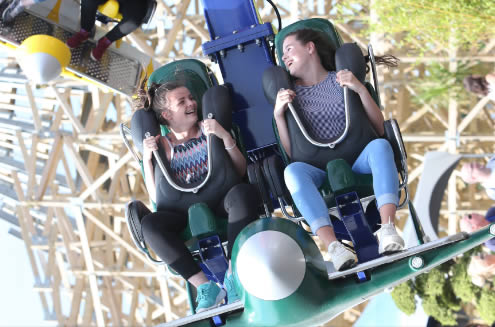 two girls looking directly at each other and smiling, as they go upside down on a theme park attraction