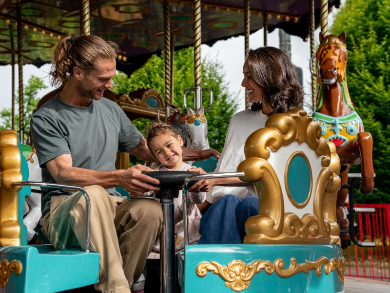 A family of three smiling and having fun on the grand carousel